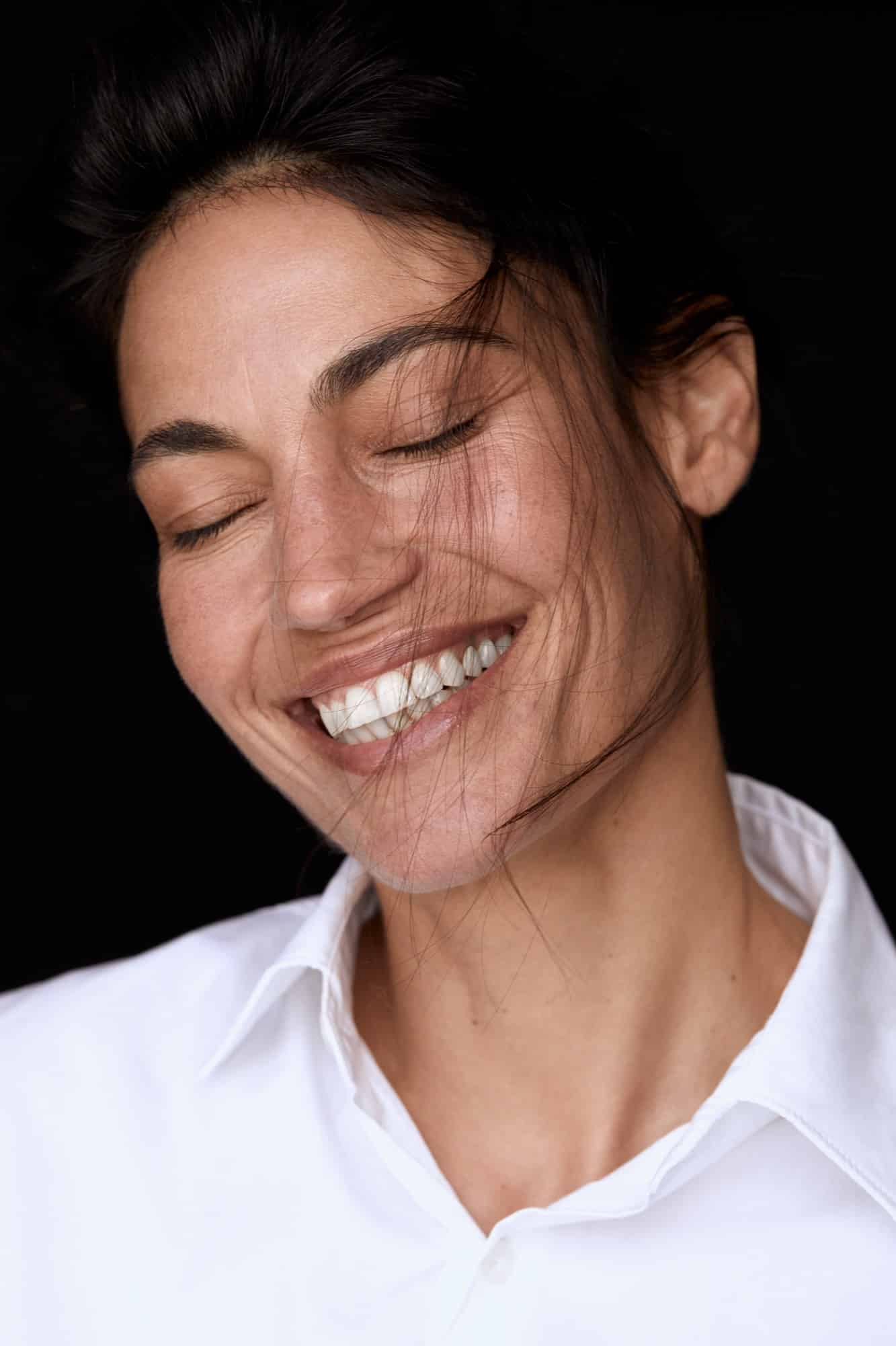 תמונת אישה מחייכת בעיניים עצומות, היא לובשת חולצה לבנה